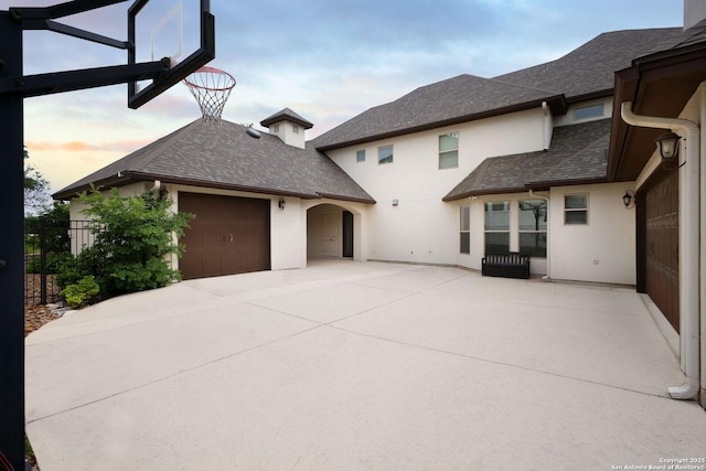 exterior space featuring an attached garage, fence, a shingled roof, and stucco siding