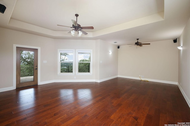 unfurnished living room featuring baseboards, a raised ceiling, ceiling fan, and dark wood-style floors