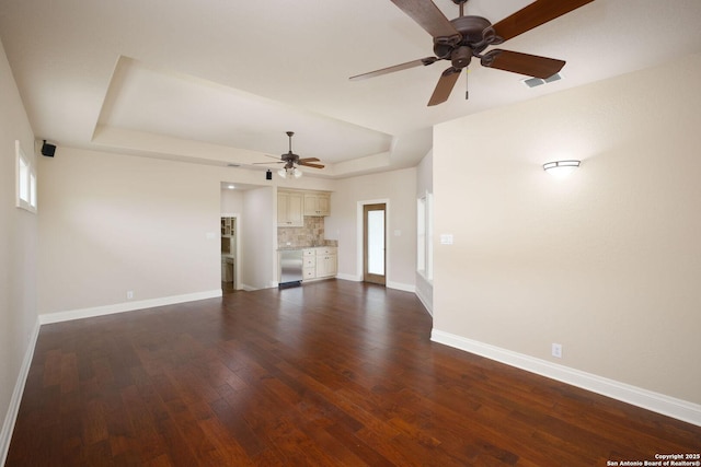 unfurnished living room featuring a raised ceiling, ceiling fan, baseboards, and dark wood-style flooring