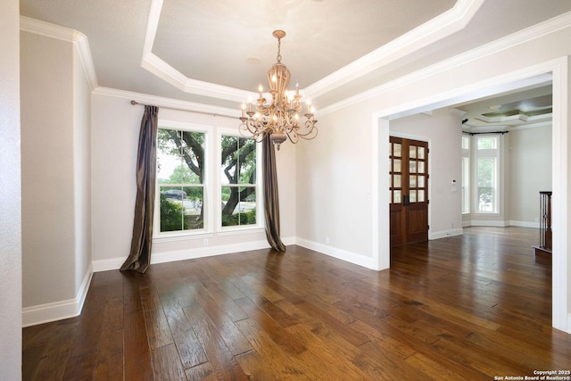 spare room with an inviting chandelier, dark wood-type flooring, a tray ceiling, and a wealth of natural light