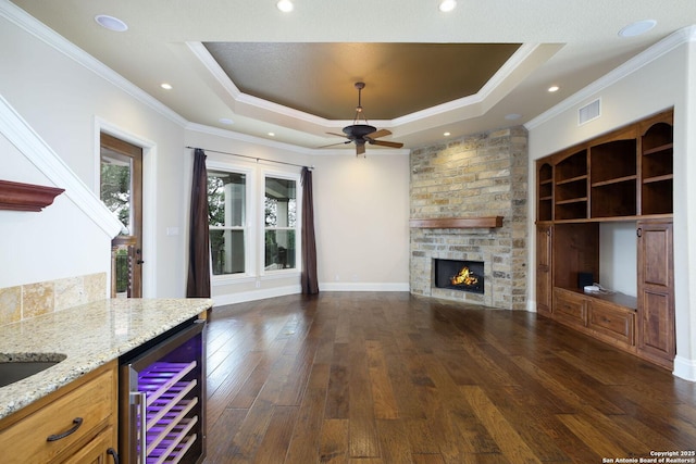 unfurnished living room featuring visible vents, a fireplace, a raised ceiling, beverage cooler, and ornamental molding
