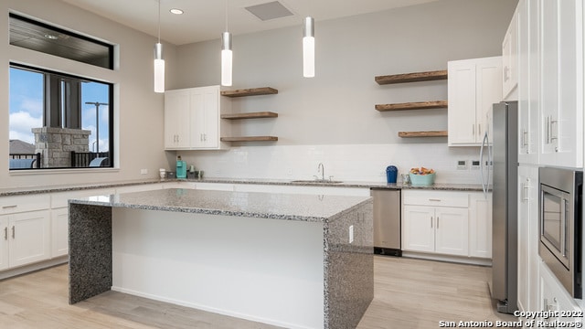 kitchen featuring stainless steel appliances, open shelves, light wood-style flooring, and a center island