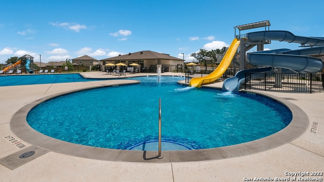 community pool with fence, a water slide, a patio area, and playground community