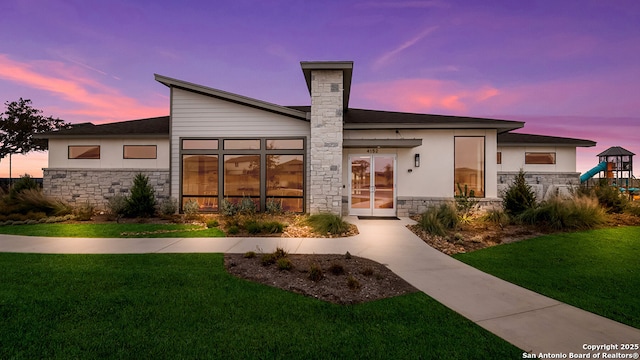back of house with a lawn, a playground, stucco siding, and stone siding