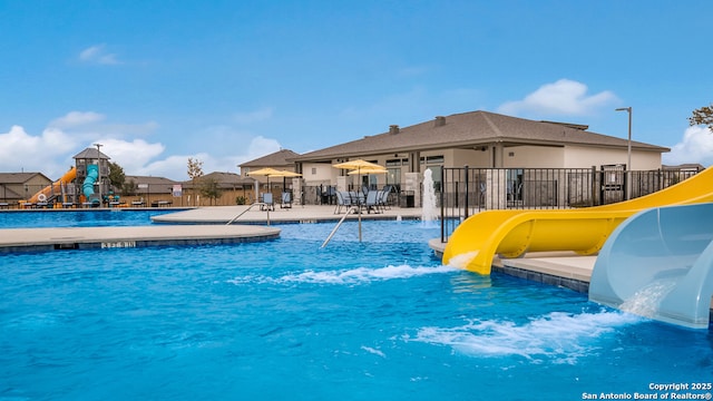 pool featuring fence, a water slide, and a patio area