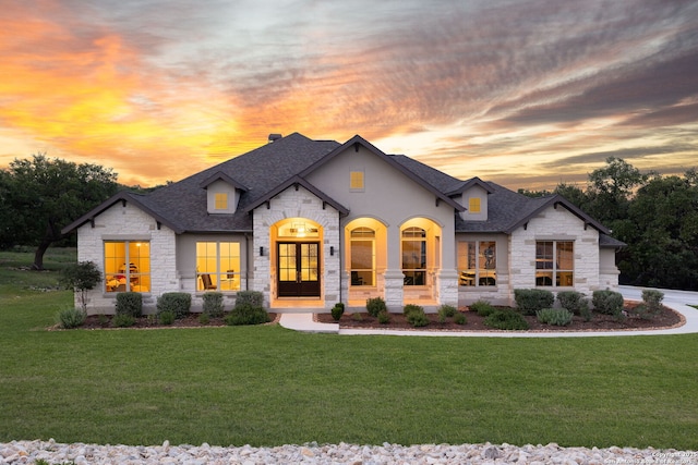 french country inspired facade with roof with shingles, a front yard, and stone siding