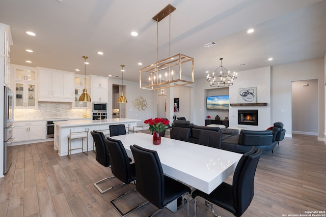 dining space with a notable chandelier, light wood-style floors, a large fireplace, recessed lighting, and visible vents