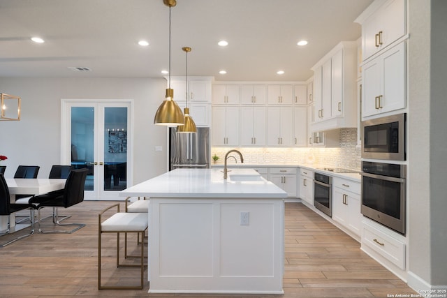 kitchen featuring french doors, appliances with stainless steel finishes, tasteful backsplash, a sink, and light wood finished floors