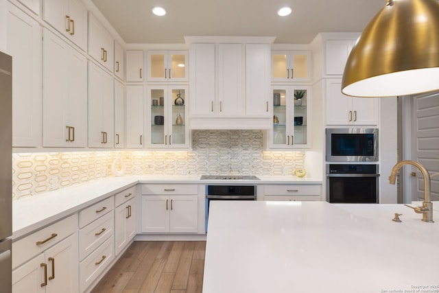 kitchen with decorative backsplash, light countertops, white cabinets, light wood-style floors, and stainless steel appliances