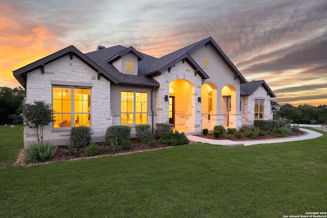 french provincial home with a shingled roof, a front yard, and stone siding