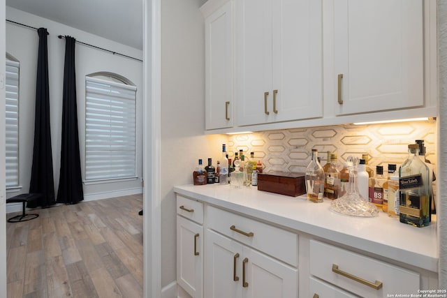 bar with a dry bar, backsplash, and light wood-style flooring