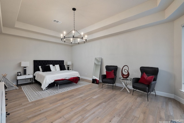 bedroom with a notable chandelier, a tray ceiling, visible vents, and light wood-type flooring