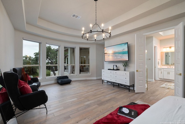 interior space featuring visible vents, light wood-type flooring, baseboards, a notable chandelier, and a tray ceiling