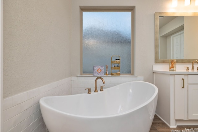 full bath with a freestanding tub, vanity, wainscoting, and tile walls