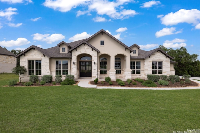 french country style house featuring a front yard, a shingled roof, stone siding, and stucco siding