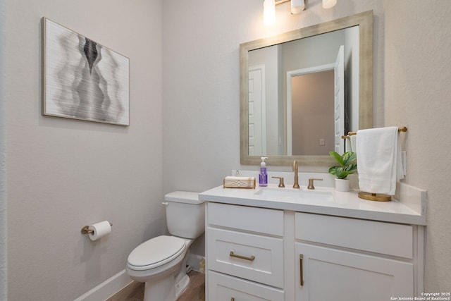 half bathroom with vanity, baseboards, wood finished floors, and toilet