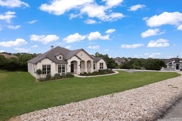 french country style house with a shingled roof, stone siding, a front yard, and a chimney