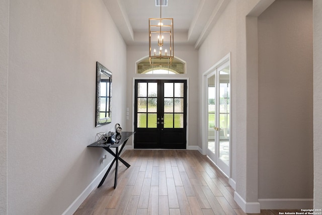 foyer featuring french doors, wood finished floors, a raised ceiling, baseboards, and a chandelier