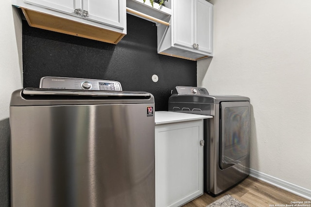 laundry room with cabinet space, separate washer and dryer, baseboards, and wood finished floors
