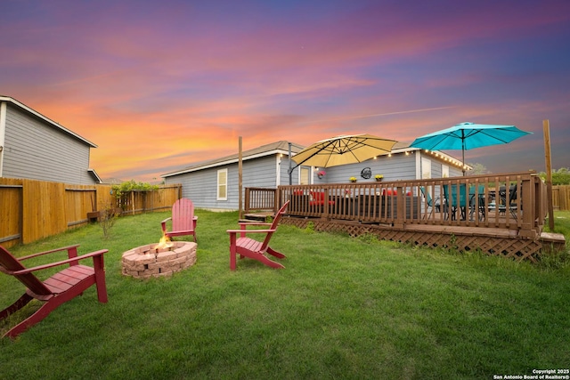 yard at dusk featuring a fenced backyard, a fire pit, and a deck