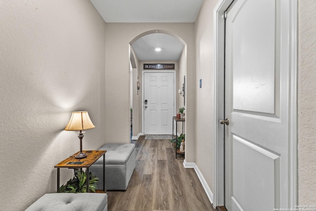 hallway featuring baseboards, arched walkways, and dark wood-style flooring