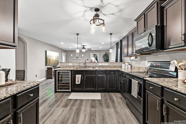 kitchen with a sink, light wood finished floors, a peninsula, wine cooler, and black appliances