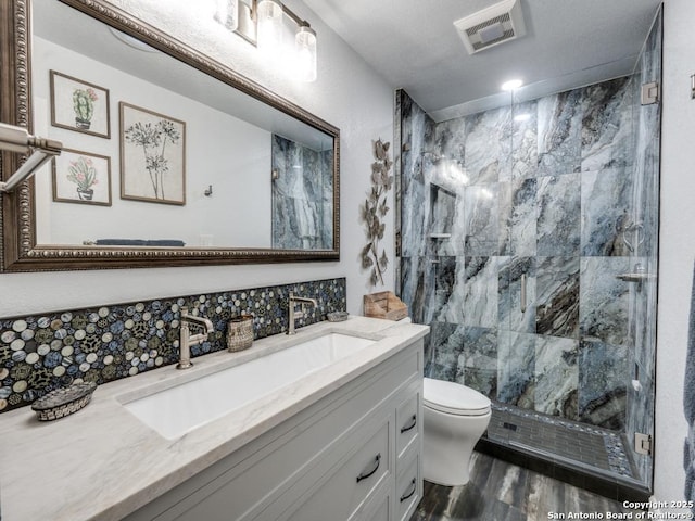 bathroom with visible vents, vanity, wood finished floors, toilet, and a marble finish shower