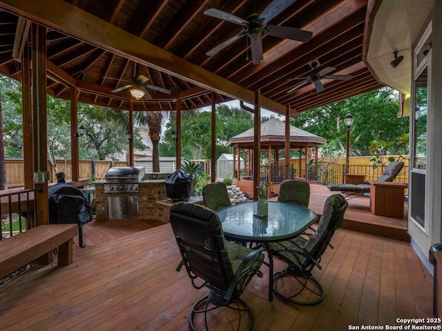 deck with a fenced backyard, area for grilling, an outdoor kitchen, a ceiling fan, and a gazebo