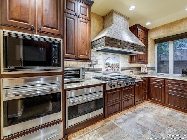 kitchen featuring premium range hood, decorative backsplash, stainless steel appliances, and light stone counters