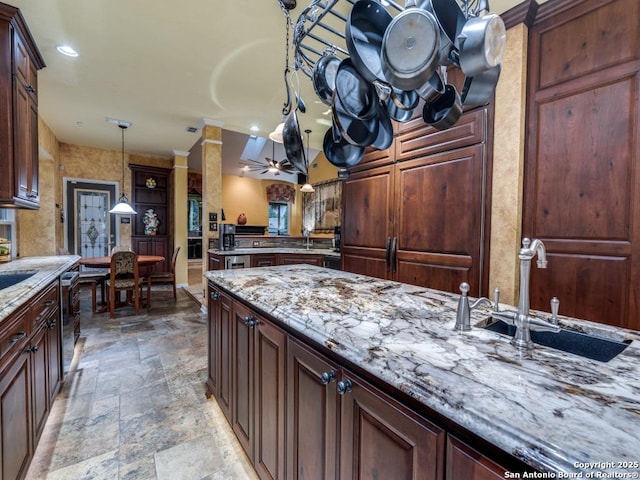 kitchen with light stone countertops, hanging light fixtures, a sink, stone finish floor, and recessed lighting