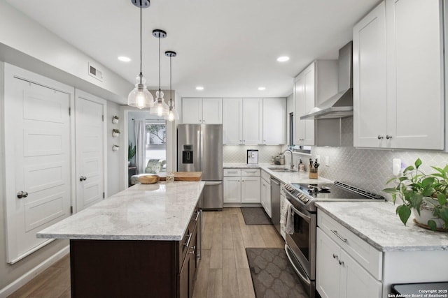 kitchen with a kitchen island, wall chimney range hood, light wood-type flooring, white cabinets, and stainless steel appliances