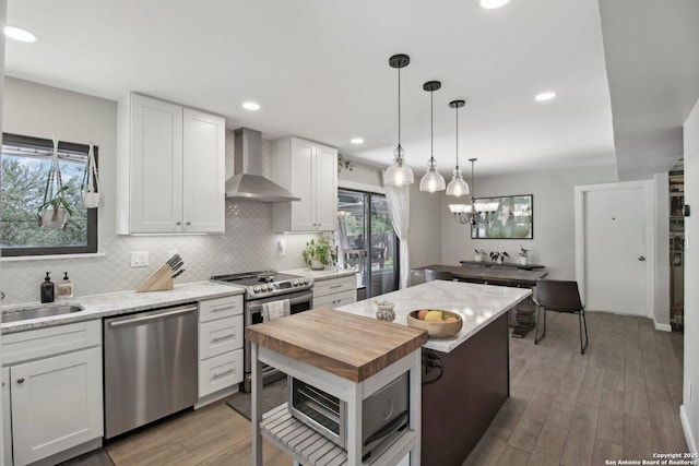 kitchen featuring wall chimney range hood, white cabinets, a sink, stainless steel appliances, and decorative backsplash