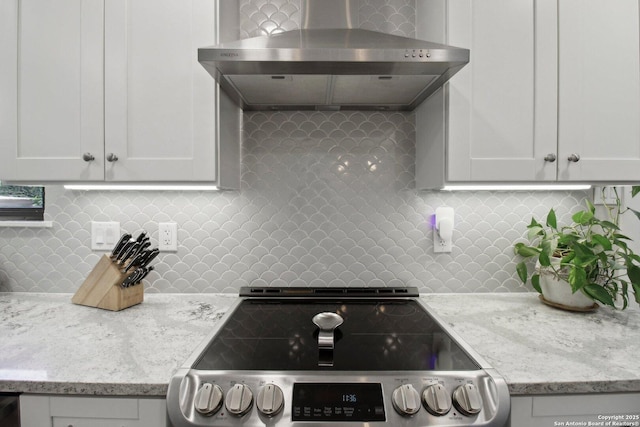 kitchen featuring tasteful backsplash, light stone countertops, wall chimney exhaust hood, stainless steel range with electric cooktop, and white cabinetry