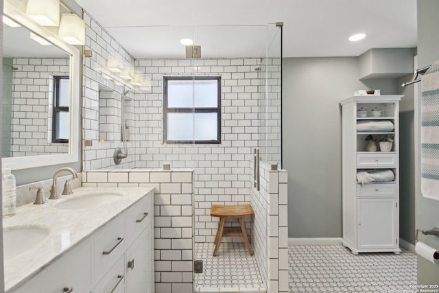 full bathroom featuring double vanity, baseboards, tiled shower, and a sink