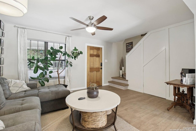 living room featuring light wood-type flooring, a ceiling fan, and stairs