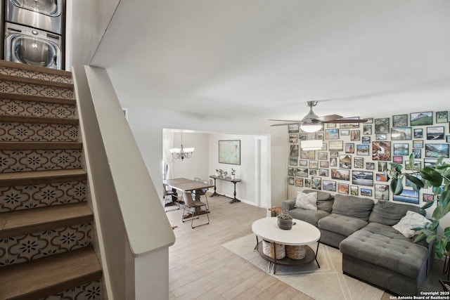 living room with stacked washer and dryer, wood finished floors, stairway, and ceiling fan with notable chandelier