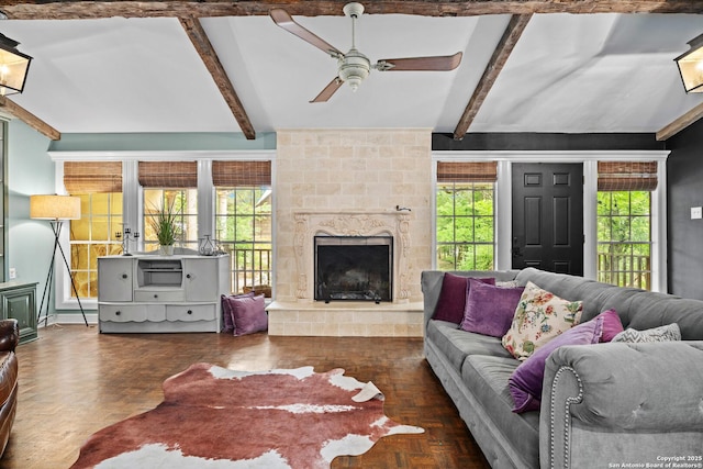 living area with ceiling fan, a healthy amount of sunlight, a fireplace, and beamed ceiling