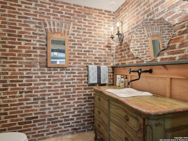 half bathroom featuring vanity, toilet, and brick wall