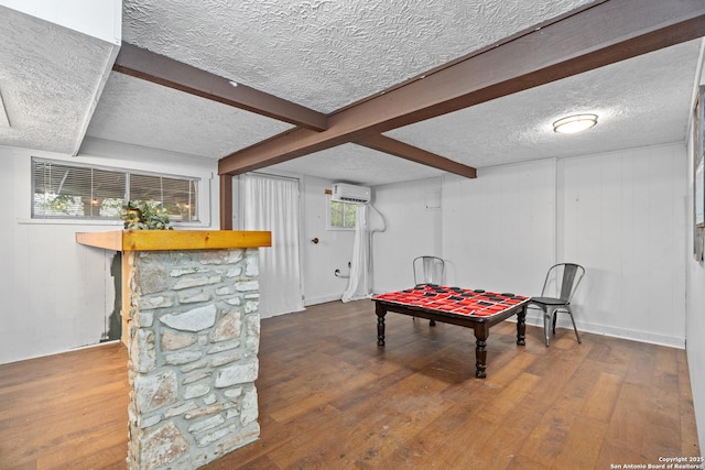 playroom with wooden walls, a textured ceiling, a wall unit AC, wood finished floors, and beamed ceiling