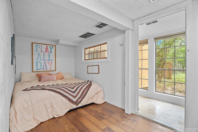 bedroom featuring visible vents, a textured ceiling, and wood finished floors