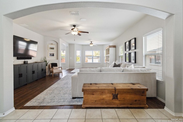 living area featuring ceiling fan, light wood finished floors, arched walkways, baseboards, and visible vents