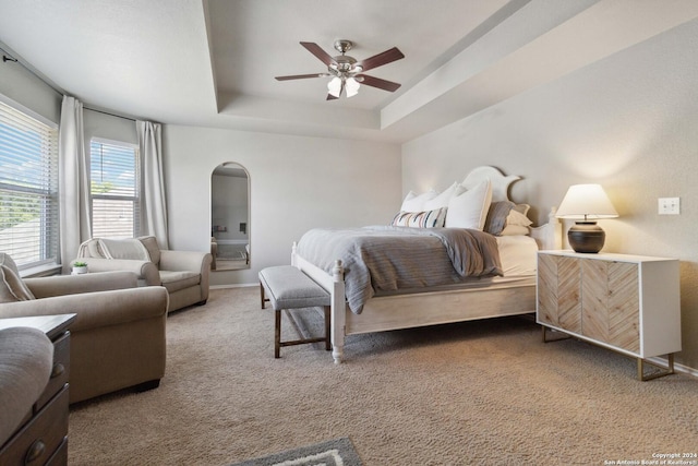 carpeted bedroom featuring baseboards, arched walkways, ceiling fan, and a tray ceiling