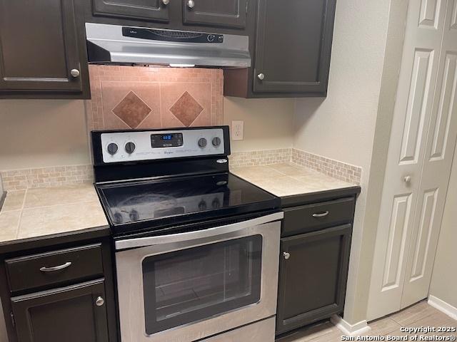 kitchen featuring light countertops, backsplash, stainless steel electric stove, and range hood