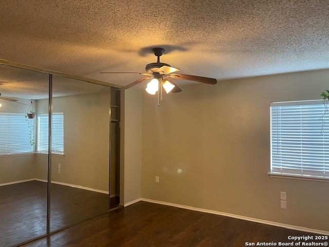 unfurnished bedroom with a ceiling fan, a textured ceiling, baseboards, a closet, and dark wood-type flooring