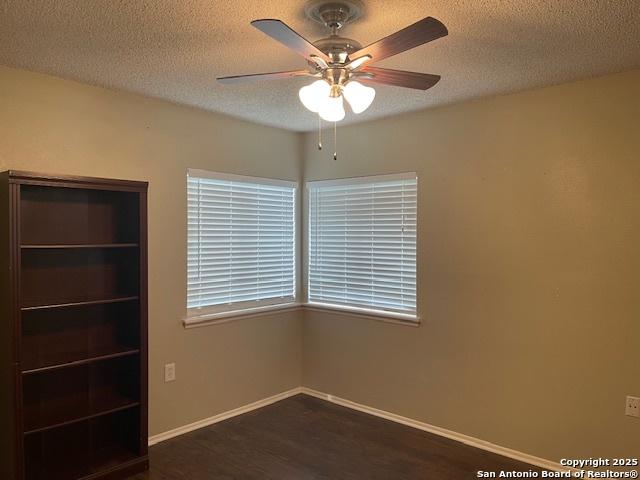 unfurnished bedroom with a textured ceiling, baseboards, dark wood finished floors, and a ceiling fan