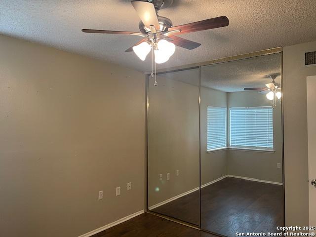 unfurnished bedroom featuring ceiling fan, a textured ceiling, baseboards, a closet, and dark wood-type flooring