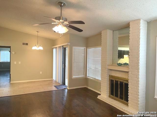 unfurnished living room featuring a textured ceiling, visible vents, and ceiling fan with notable chandelier