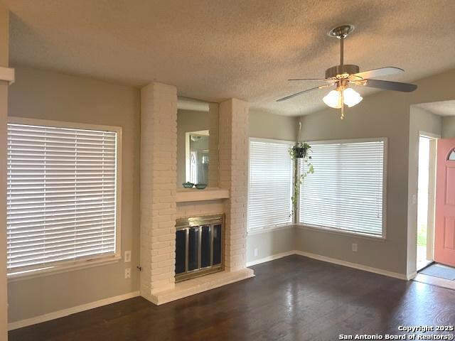 unfurnished living room featuring ceiling fan, a fireplace, a textured ceiling, and wood finished floors