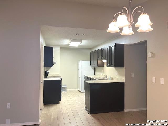 kitchen with light wood-type flooring, light countertops, baseboards, freestanding refrigerator, and a chandelier