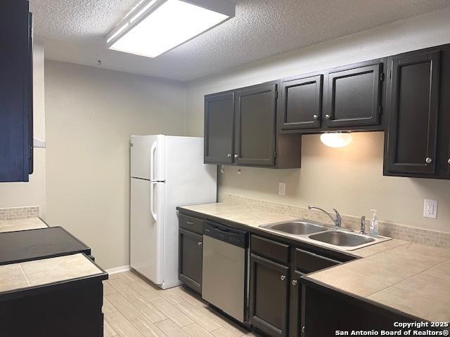 kitchen featuring stainless steel dishwasher, light wood-style floors, tile countertops, a textured ceiling, and a sink